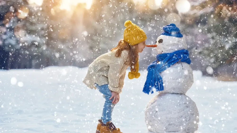 girl playing with snowman on a snowy winter walk